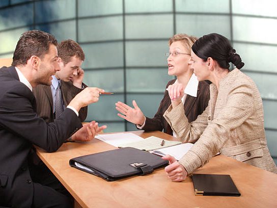 Mediation tussen bedrijven – gesprekssituatie Vijf professionals in gesprek tijdens een zakelijke vergadering aan een tafel.